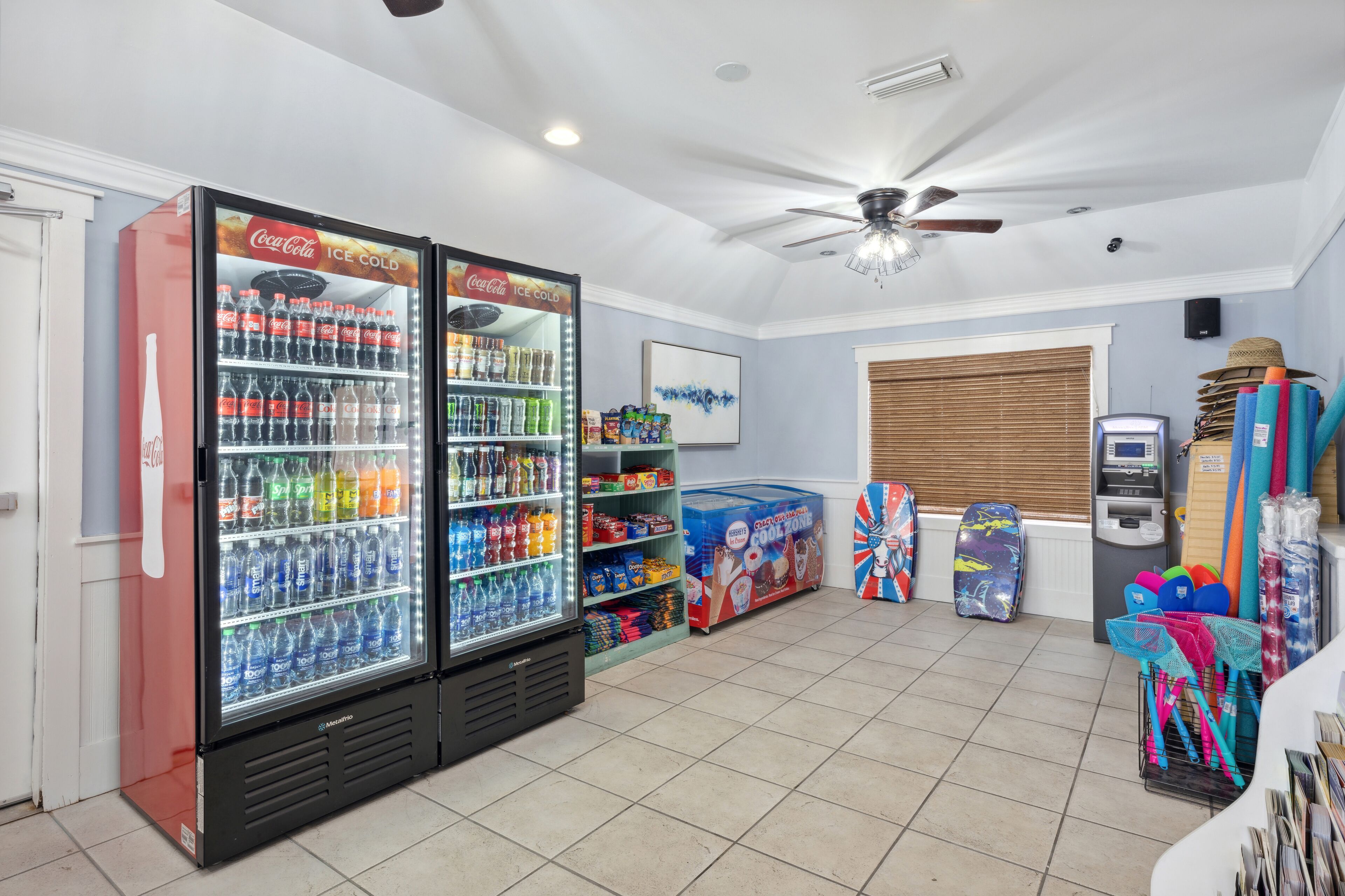 A room with two Coca-Cola refrigerators stocked with beverages, a ceiling fan, and various items on shelves.