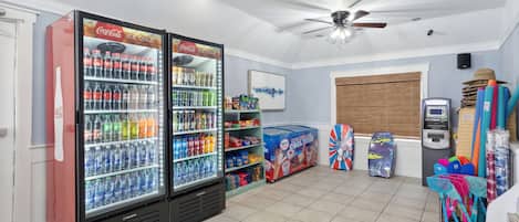 Una habitación con dos refrigeradores de Coca-Cola llenos de bebidas, un ventilador de techo y varios objetos en estantes.