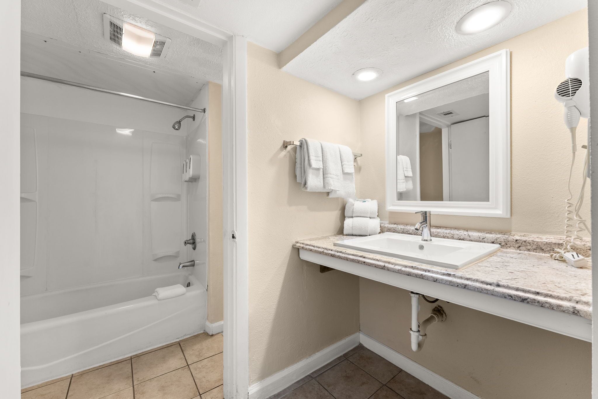 A bathroom with a bathtub, a sink, a mirror, and a hairdryer.