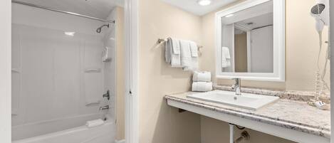 A bathroom with a bathtub, a sink, a mirror, and a hairdryer.