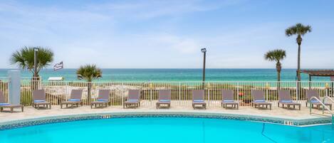 Área à beira da piscina com espreguiçadeiras e vista para o mar.