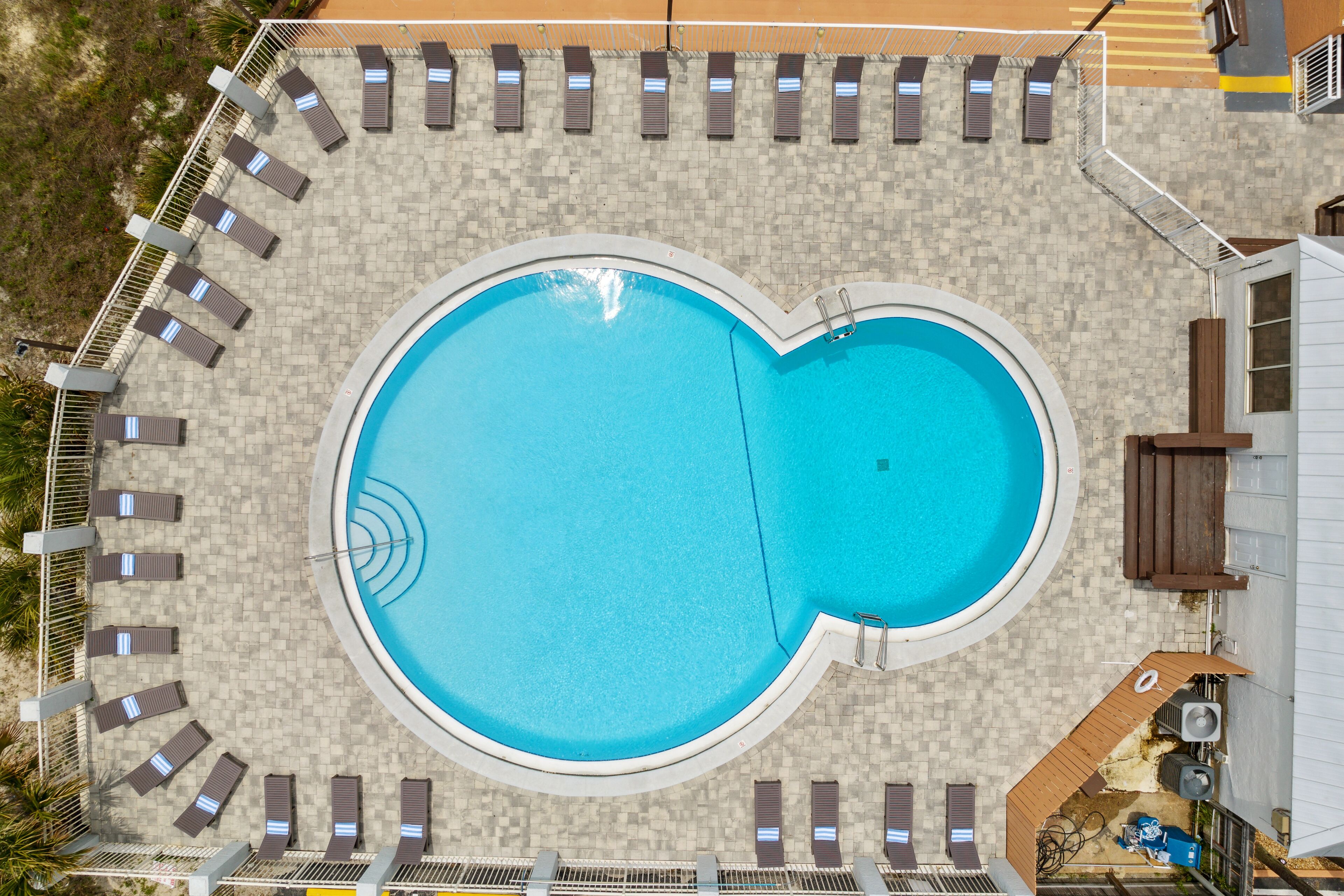 Una piscina grande y ovalada, rodeada de sillones de descanso y una terraza con baldosas.