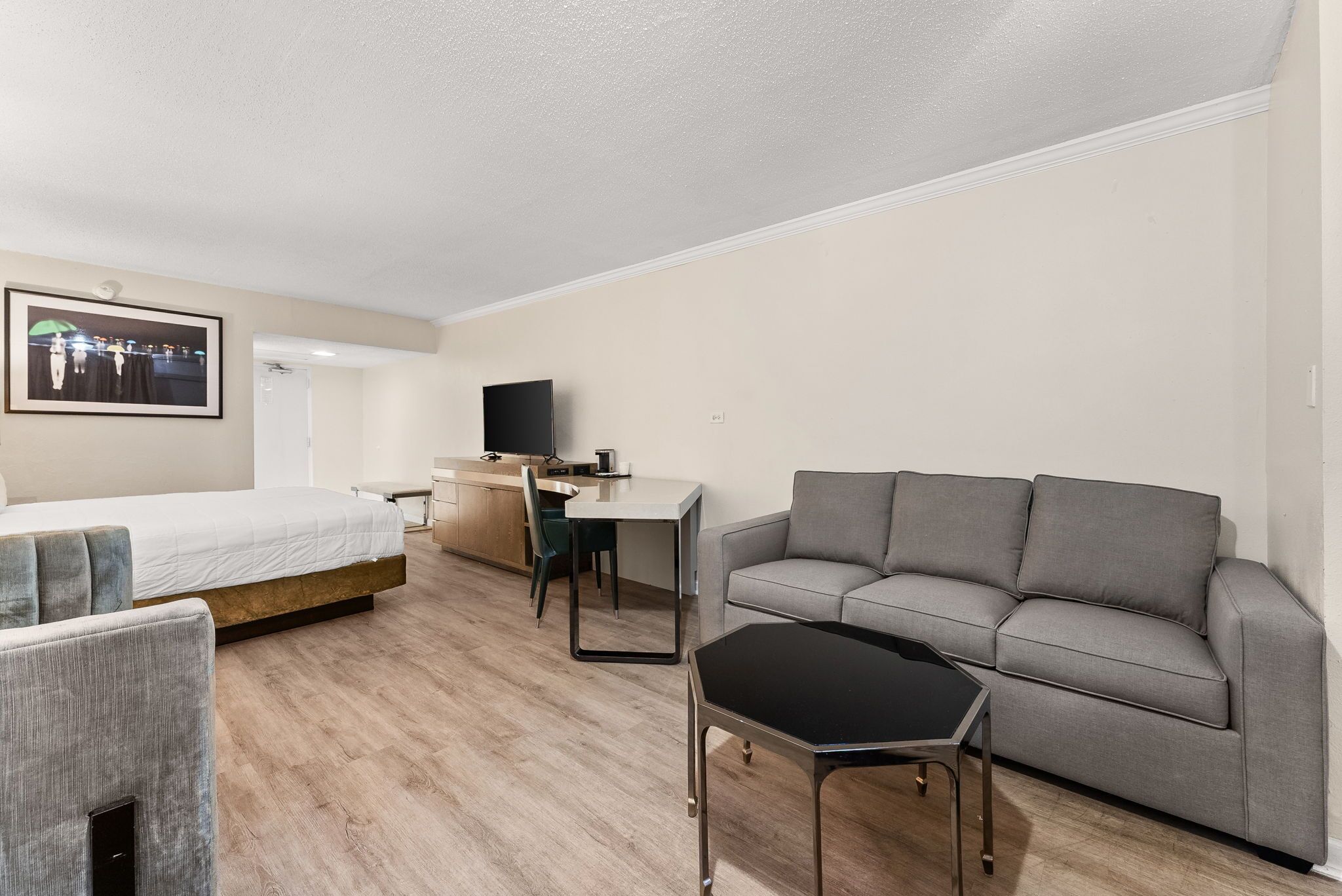 Et moderne hotelværelse med en seng, en grå sofa, et lille bord, et fjernsyn og et billede i ramme på væggen.