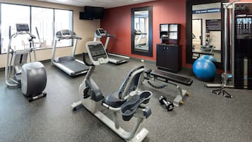 Un gimnasio con cintas de correr, elíptica, banco de pesas y pelotas de ejercicio.