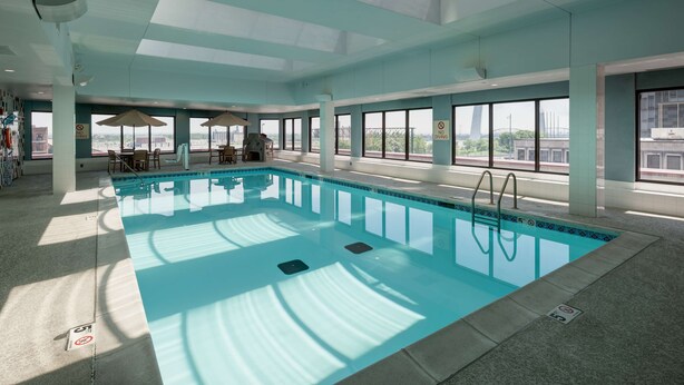 An indoor swimming pool with clear glass ceilings, large windows, and a sunlit area with umbrellas. - Hampton Inn St. Louis-Downtown (At the Gateway Arch) (St. Louis)