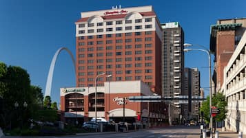 Ein Hotel mit einer markanten Bogenstruktur im Hintergrund, einem großen Schild für Hampton Inn und einem Schild für das Restaurant TGI Friday's.