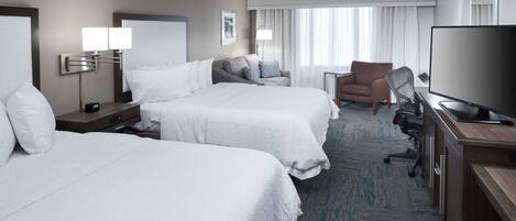 A hotel room with two beds, a desk with a TV, a chair, and a lamp.