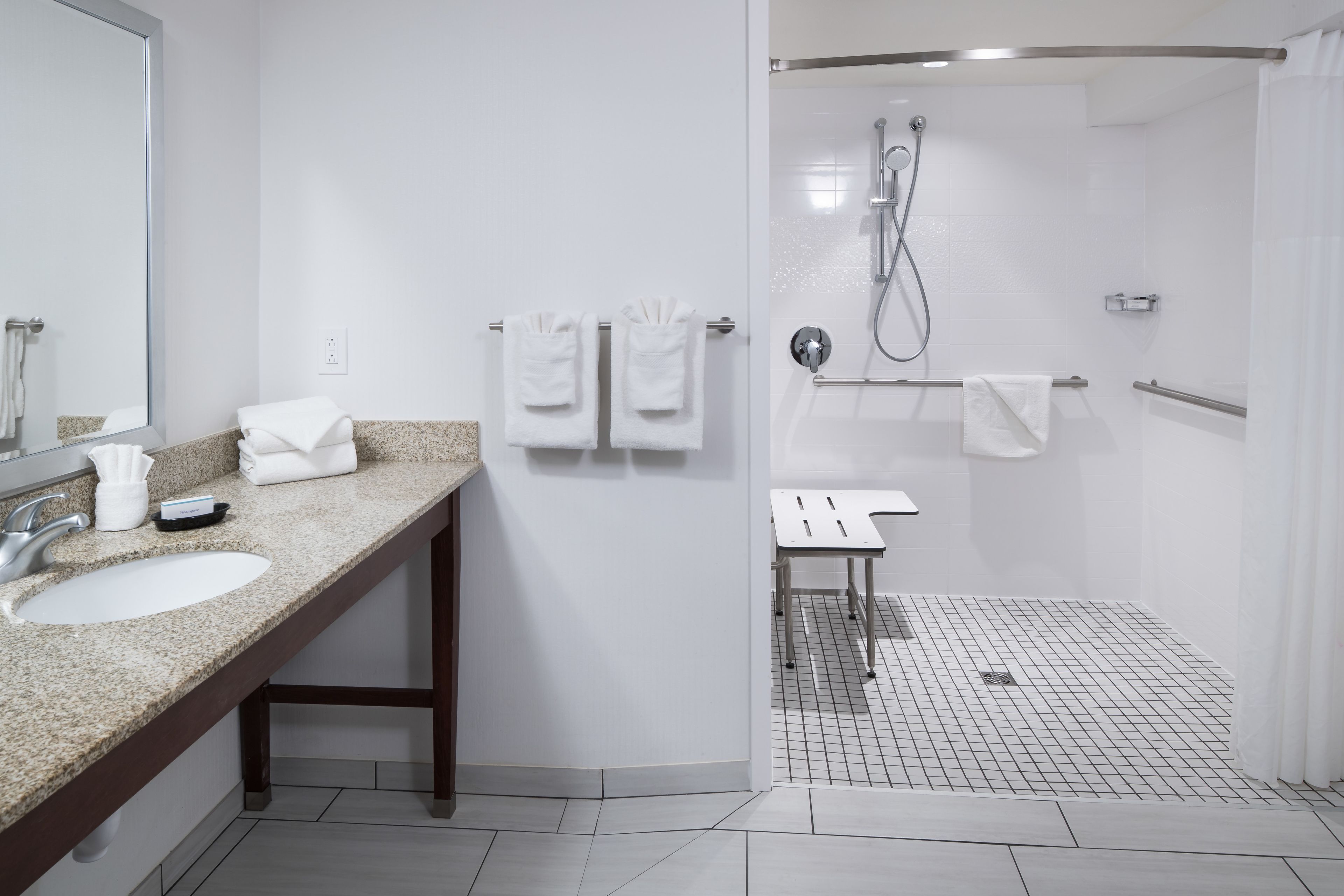 A modern bathroom with a granite countertop, a sink, a mirror, and a walk-in shower with a glass door.