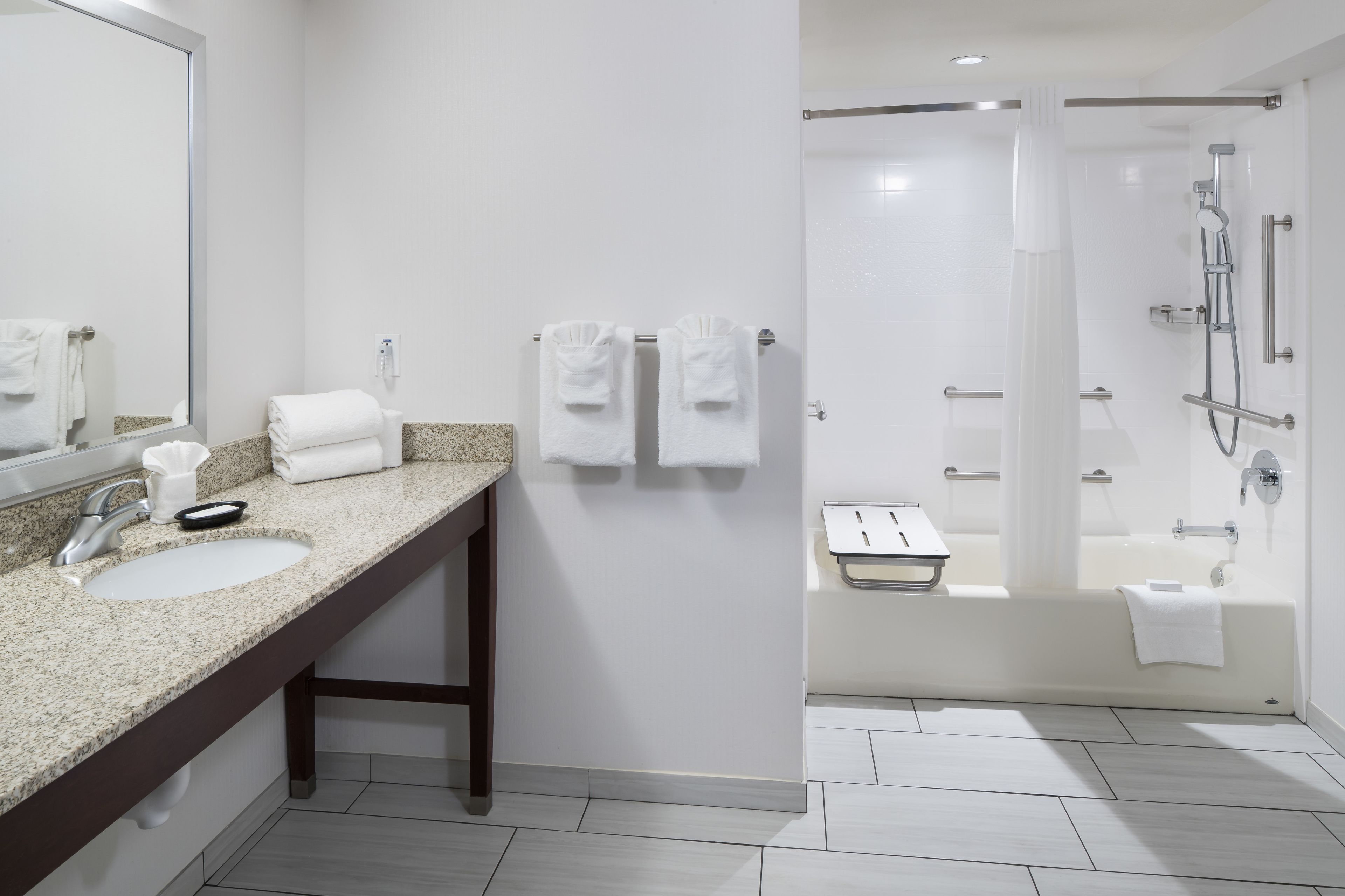 Une salle de bain moderne avec un lavabo surmonté d’un plan de travail en granit, un miroir et un espace douche doté d’une porte en verre.