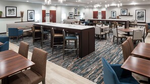 A hotel dining area with multiple tables and chairs, a central island, and pendant lighting. - Hampton Inn St. Louis-Downtown (At the Gateway Arch) (St. Louis)
