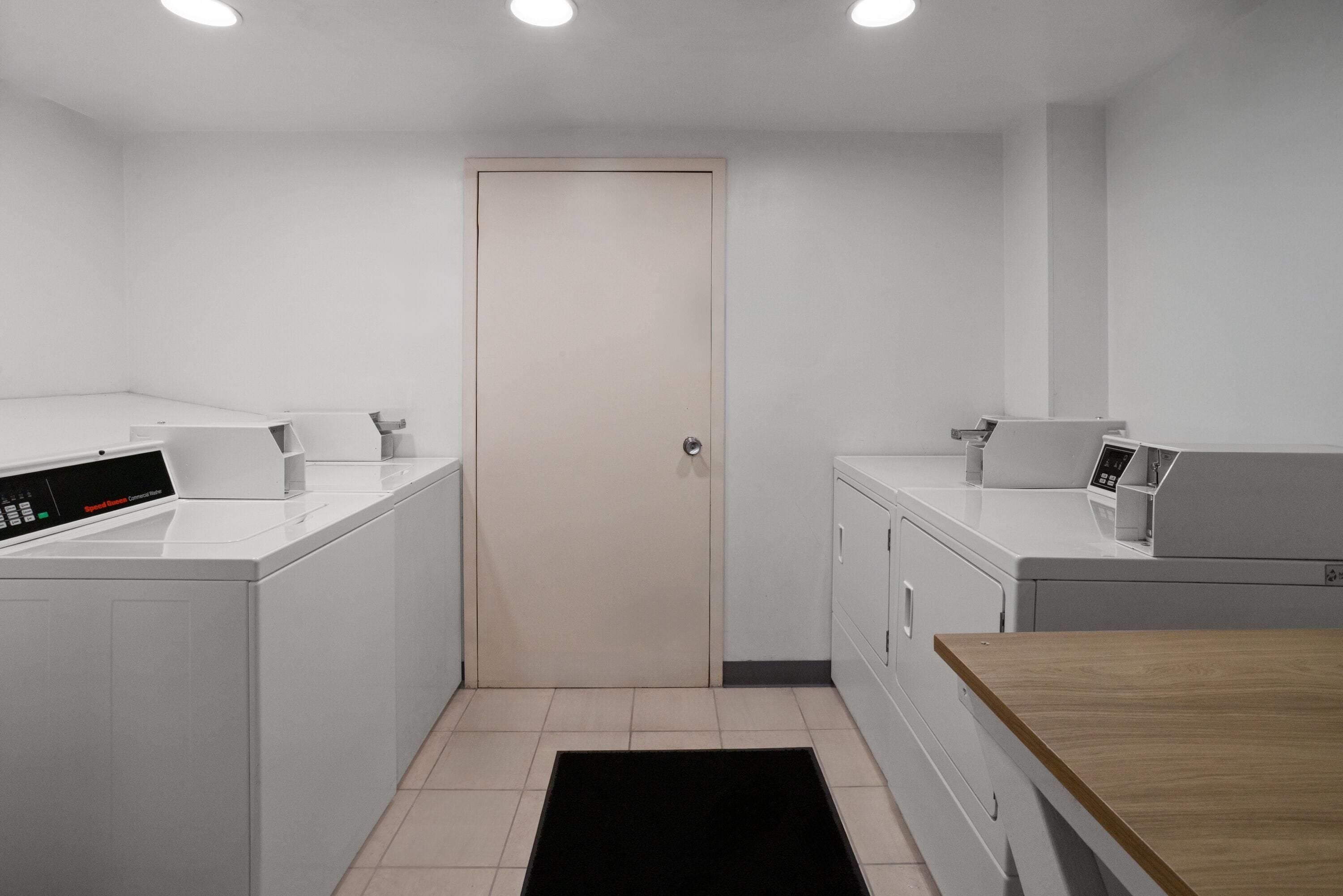 Una sala de lavandería con dos lavadoras, una secadora y una mesa de madera.