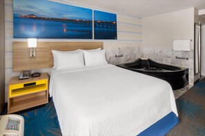 Une chambre d’hôtel comprenant un lit, une table de chevet, un bureau, une lampe de bureau, un téléphone, une baignoire et une œuvre d’art accrochée au mur.