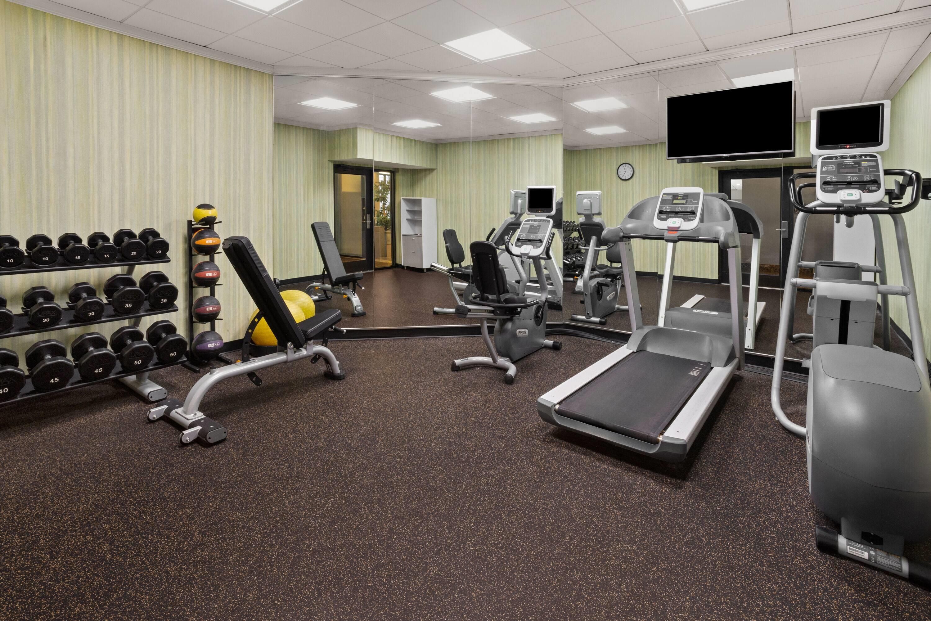 Une salle de sport équipée de divers appareils d’exercice, notamment des tapis de course, un banc de développé couché et des haltères.
