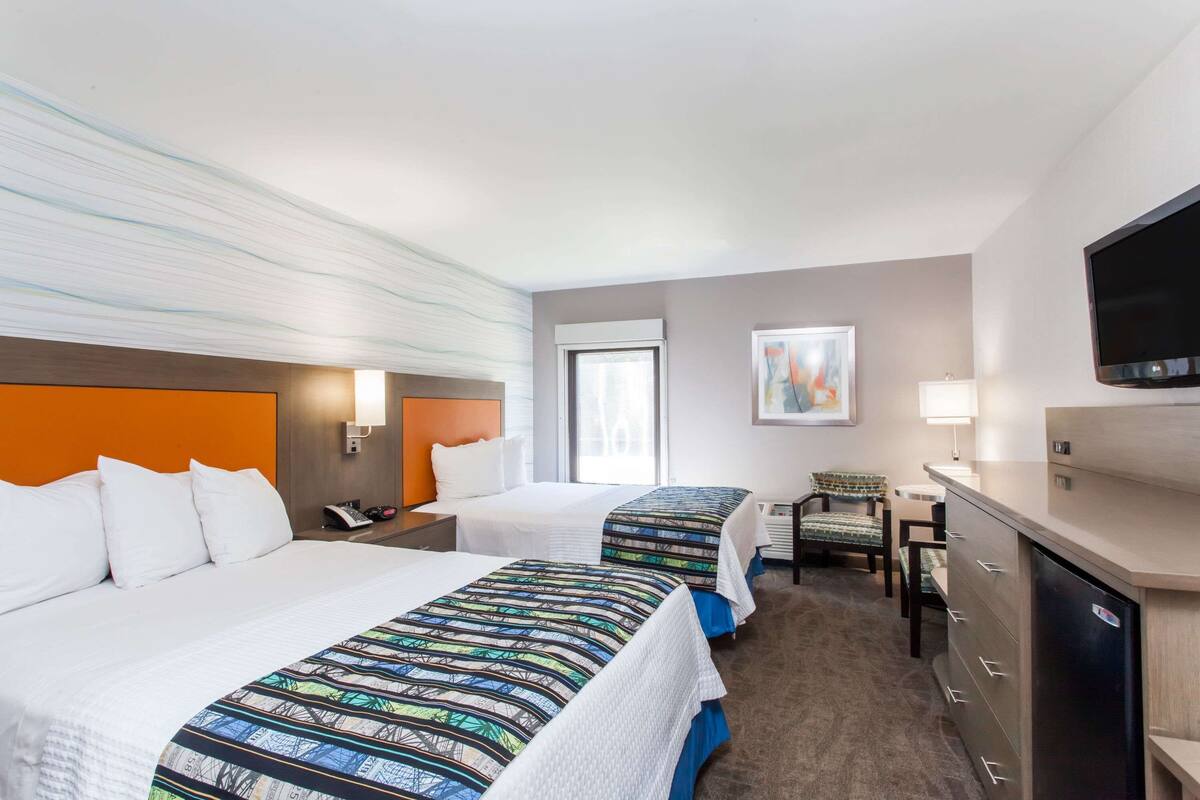 A hotel room with two beds, a desk, a chair, a TV, and a window.