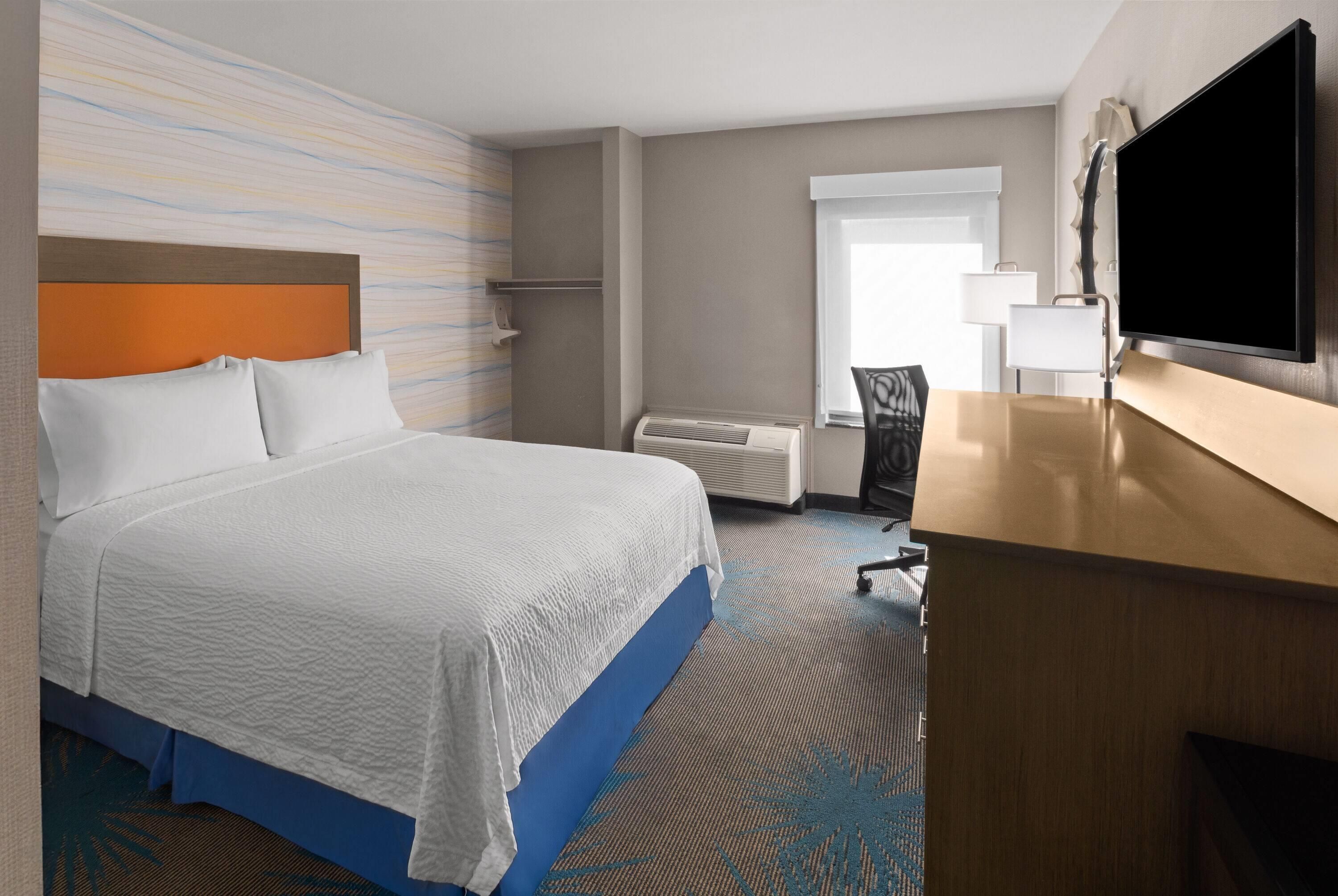A hotel room with a bed, a desk, a television, and a window.