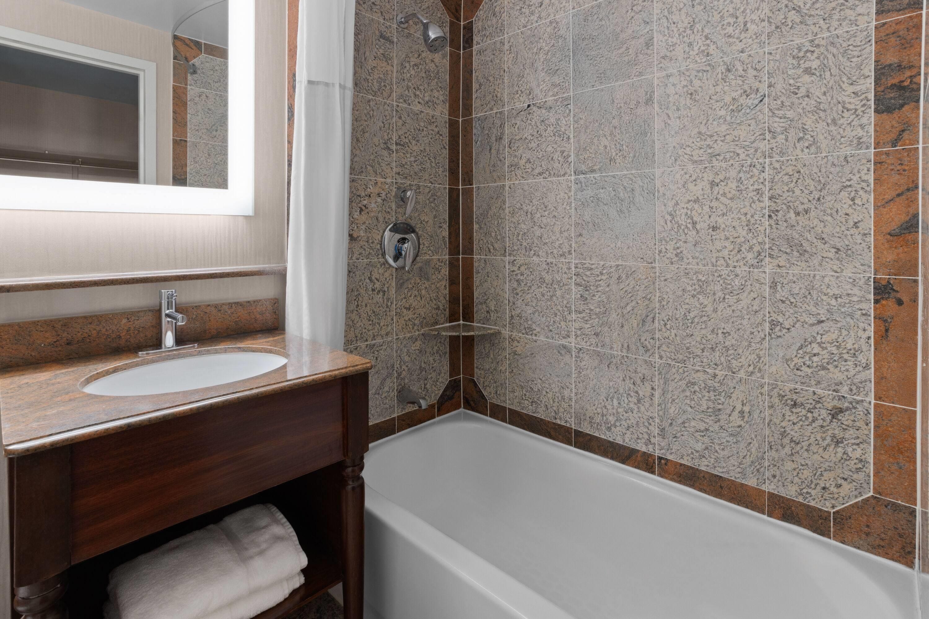 A bathroom with a white bathtub, a wooden vanity with a sink, and a shower area with a glass door.