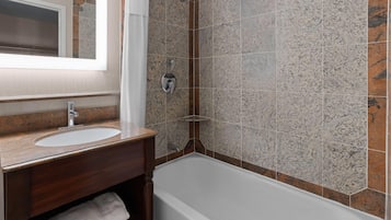 A bathroom with a white bathtub, a wooden vanity with a sink, and a shower area with a glass door.