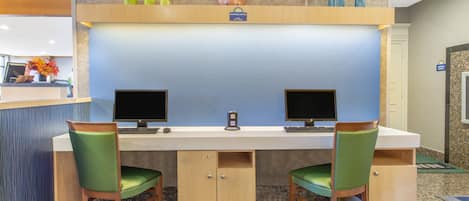 A reception desk with two monitors, a clock, and a sign indicating a business center.
