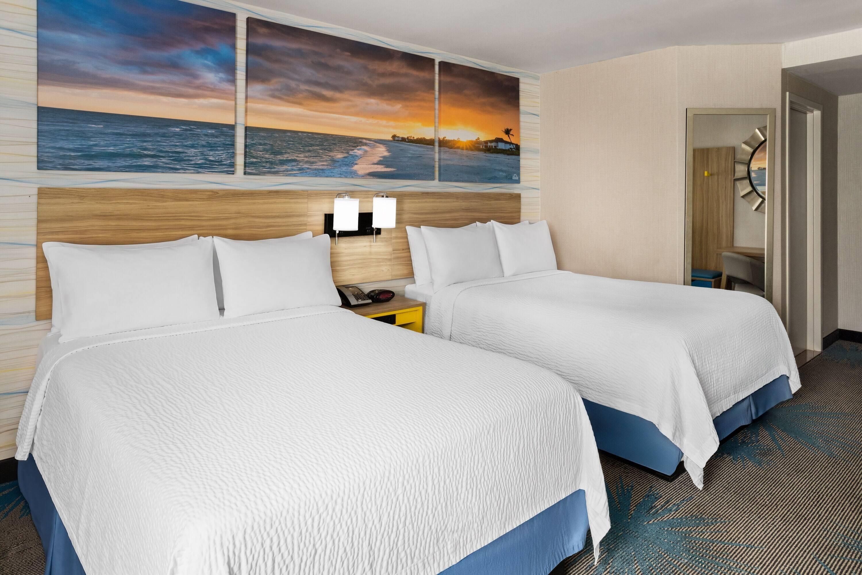 Una camera d'albergo con due letti, un comodino e un quadro raffigurante un tramonto sull'oceano.