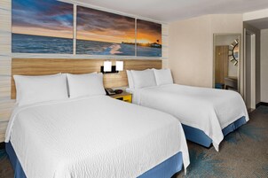 Habitación de hotel con dos camas, una mesita de noche y un cuadro de una puesta de sol sobre el océano.