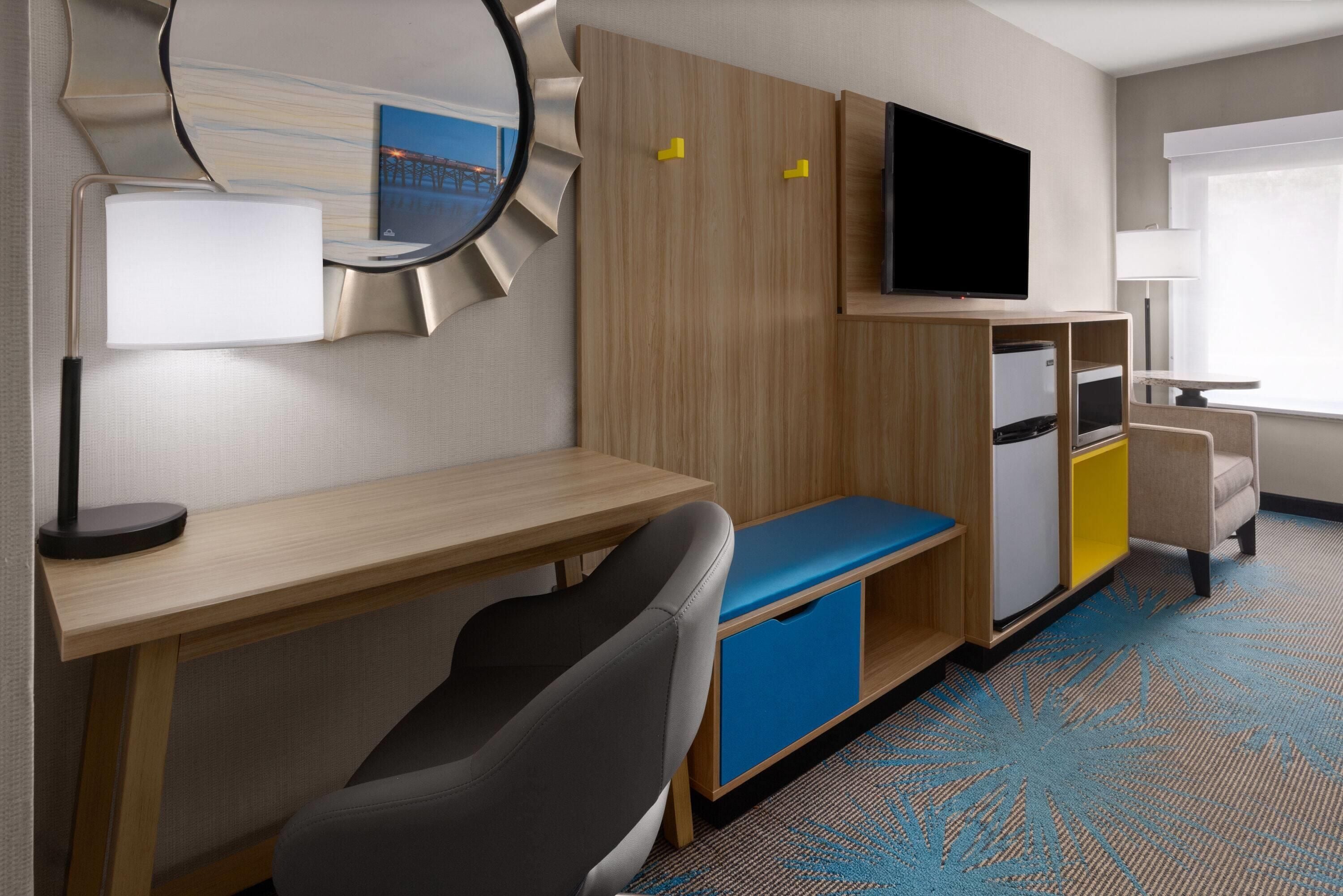 Una habitación de hotel con escritorio, silla, cama, televisor y un refrigerador pequeño.