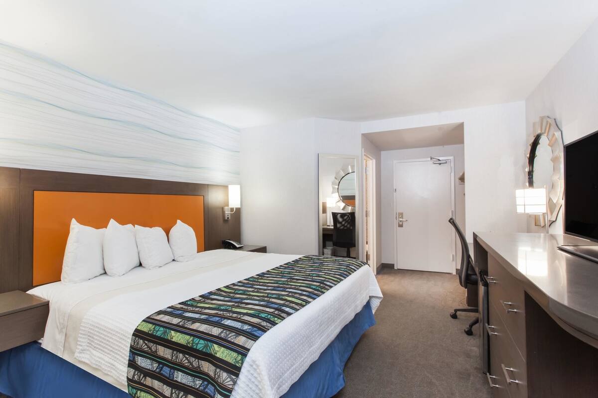 A hotel room with a bed, a desk, a chair, and a television.