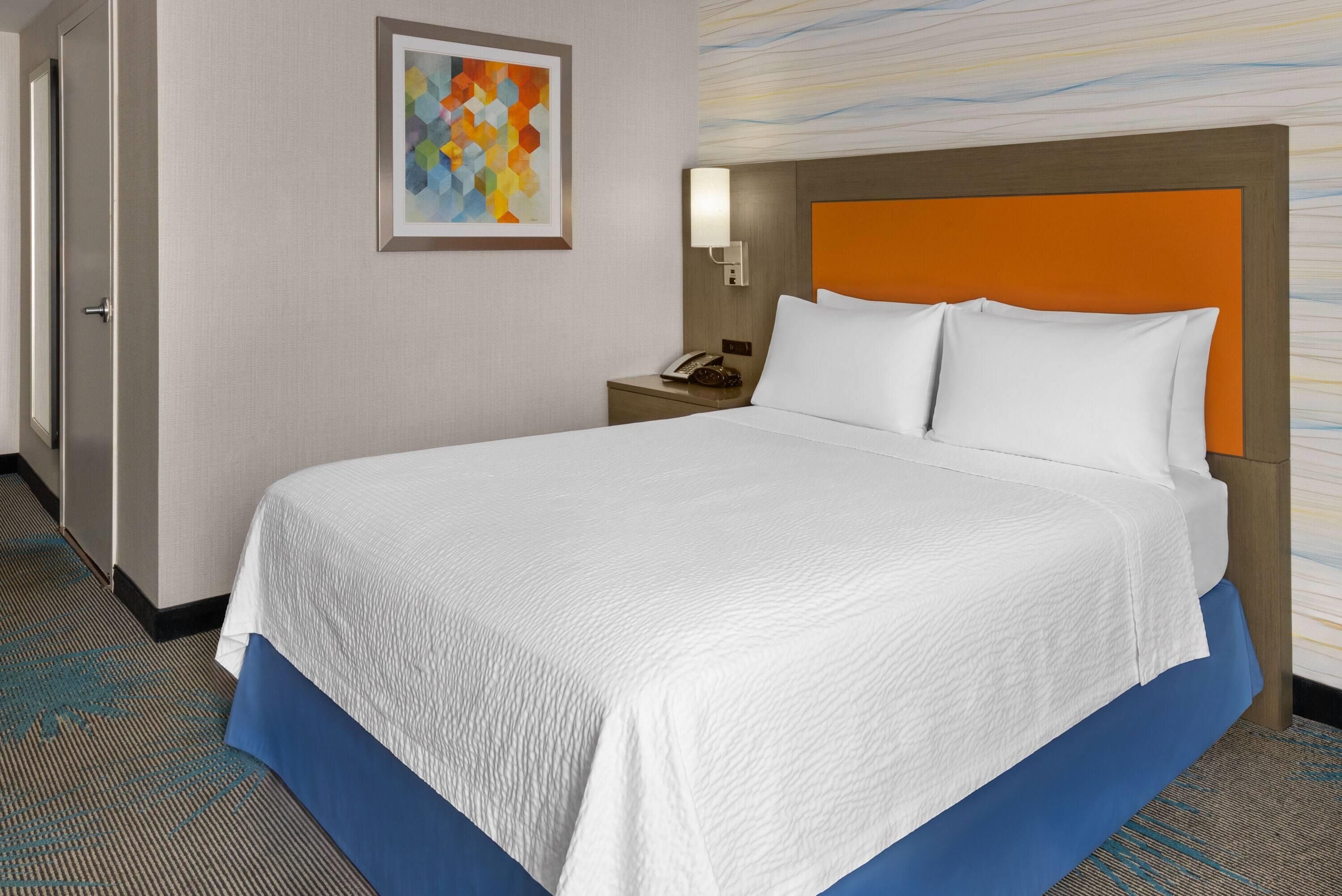 Une chambre d’hôtel avec un grand lit, une table de chevet, un téléphone et un tableau au mur.