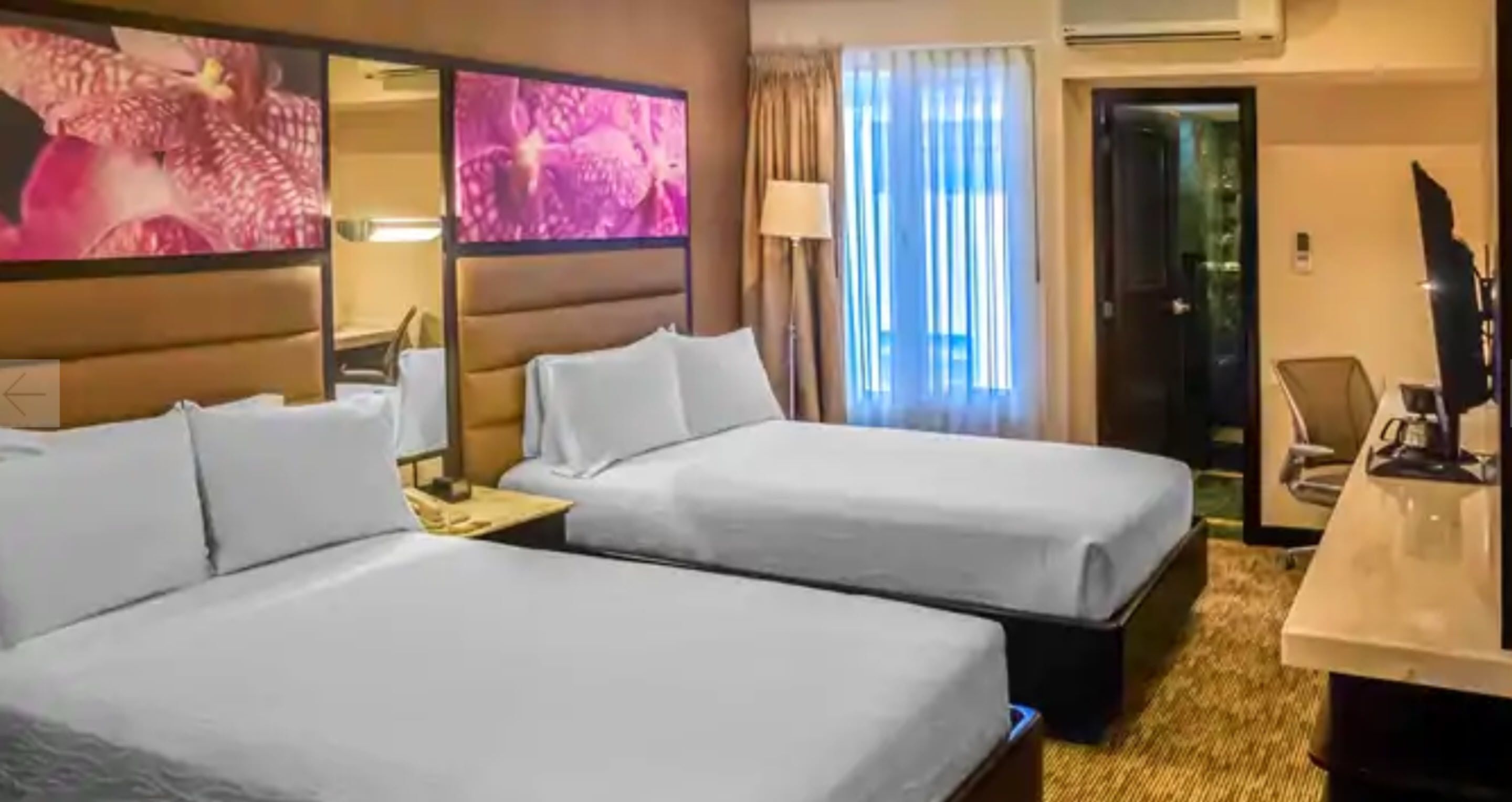 Habitación de hotel con dos camas, un escritorio, una silla y un televisor.