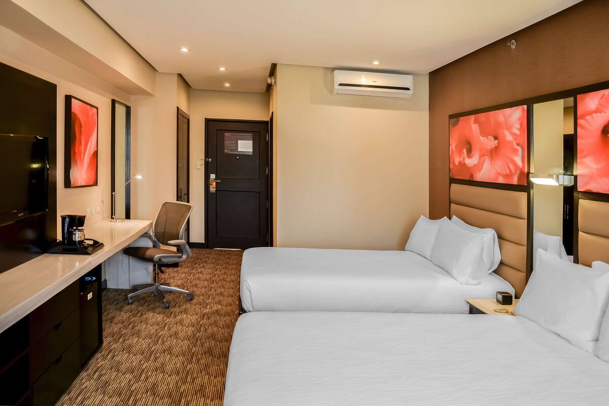 Een hotelkamer met twee bedden, een bureau, een stoel en een televisie.