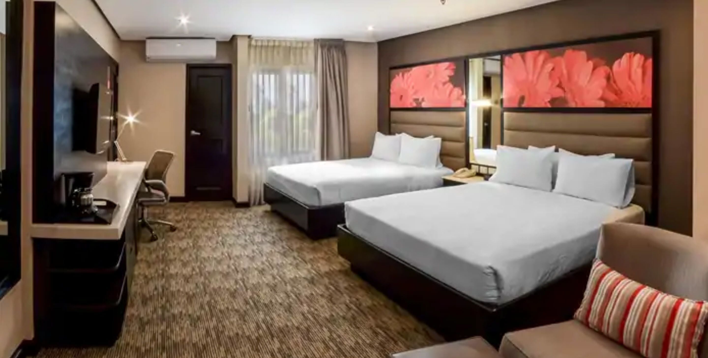 A hotel room with two beds, a desk, a chair, and a large floral artwork on the wall.