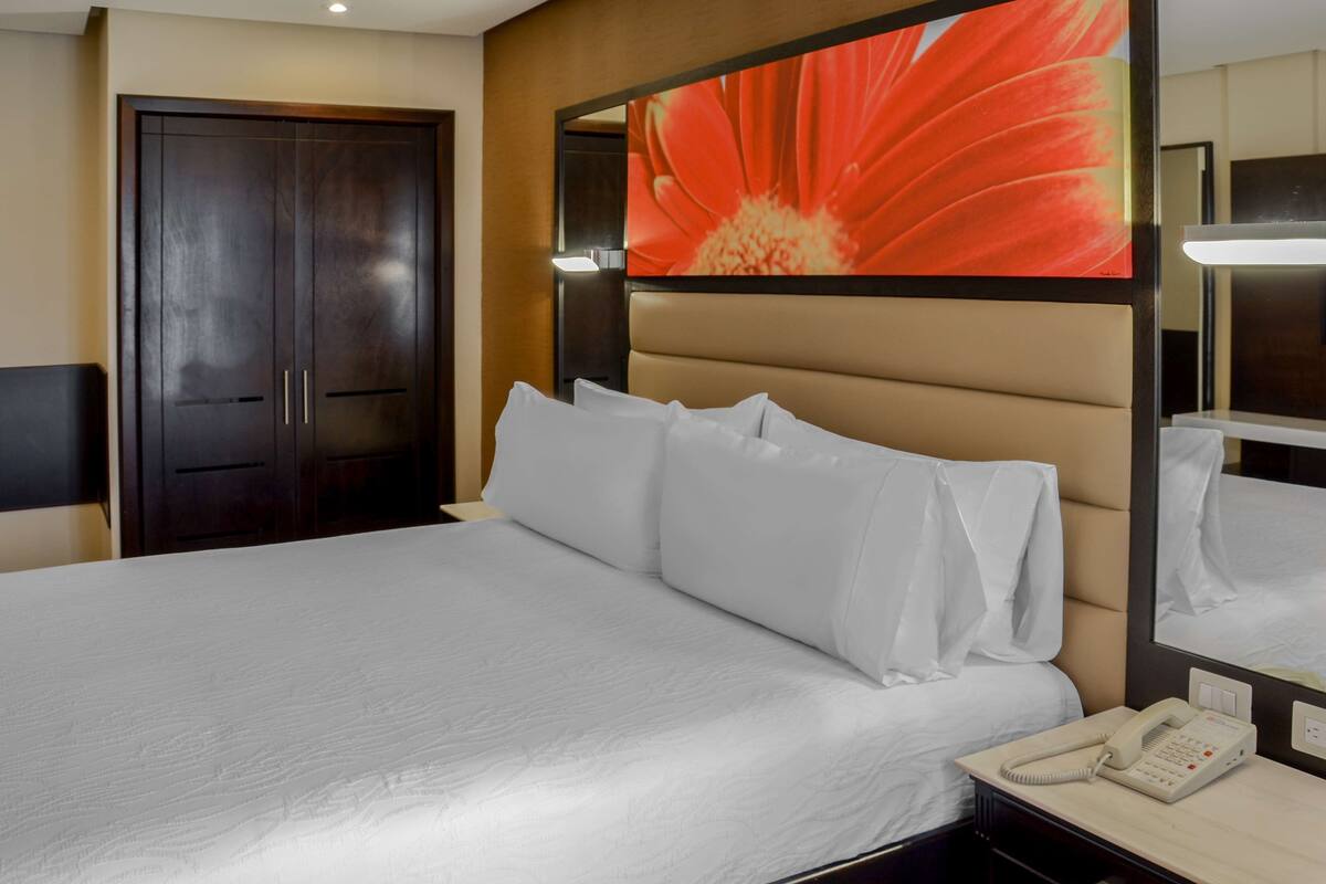 Een hotelkamer met een groot bed, een telefoon op het nachtkastje en een spiegel aan de muur.