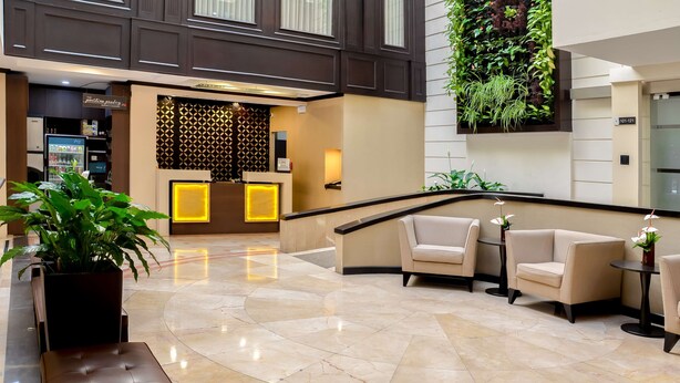 A hotel lobby with a reception desk, seating area, and a green vertical garden. - Hilton Garden Inn Guatemala City (Guatemala City)