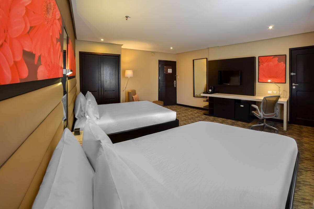 Een hotelkamer met twee bedden, een bureau, een televisie en een grote spiegel.