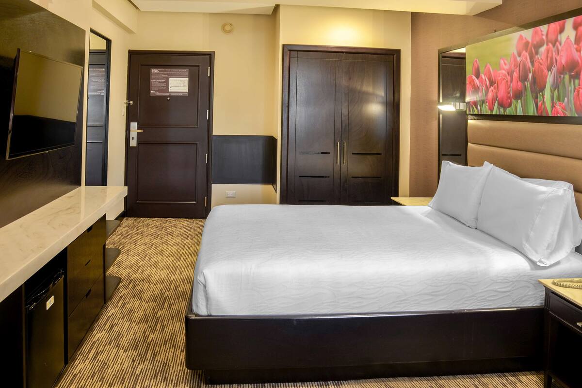 Hotelkamer met een groot bed, een flatscreen televisie, een schilderij van tulpen en een deur met een bordje.