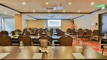 Uma sala de conferências com várias mesas e cadeiras, uma tela de projetor exibindo o logotipo do Hilton Garden Inn e a bandeira de Guatemala.