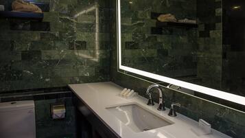 Un baño moderno con un espejo grande, un lavabo blanco y baldosas de mármol verde oscuro.