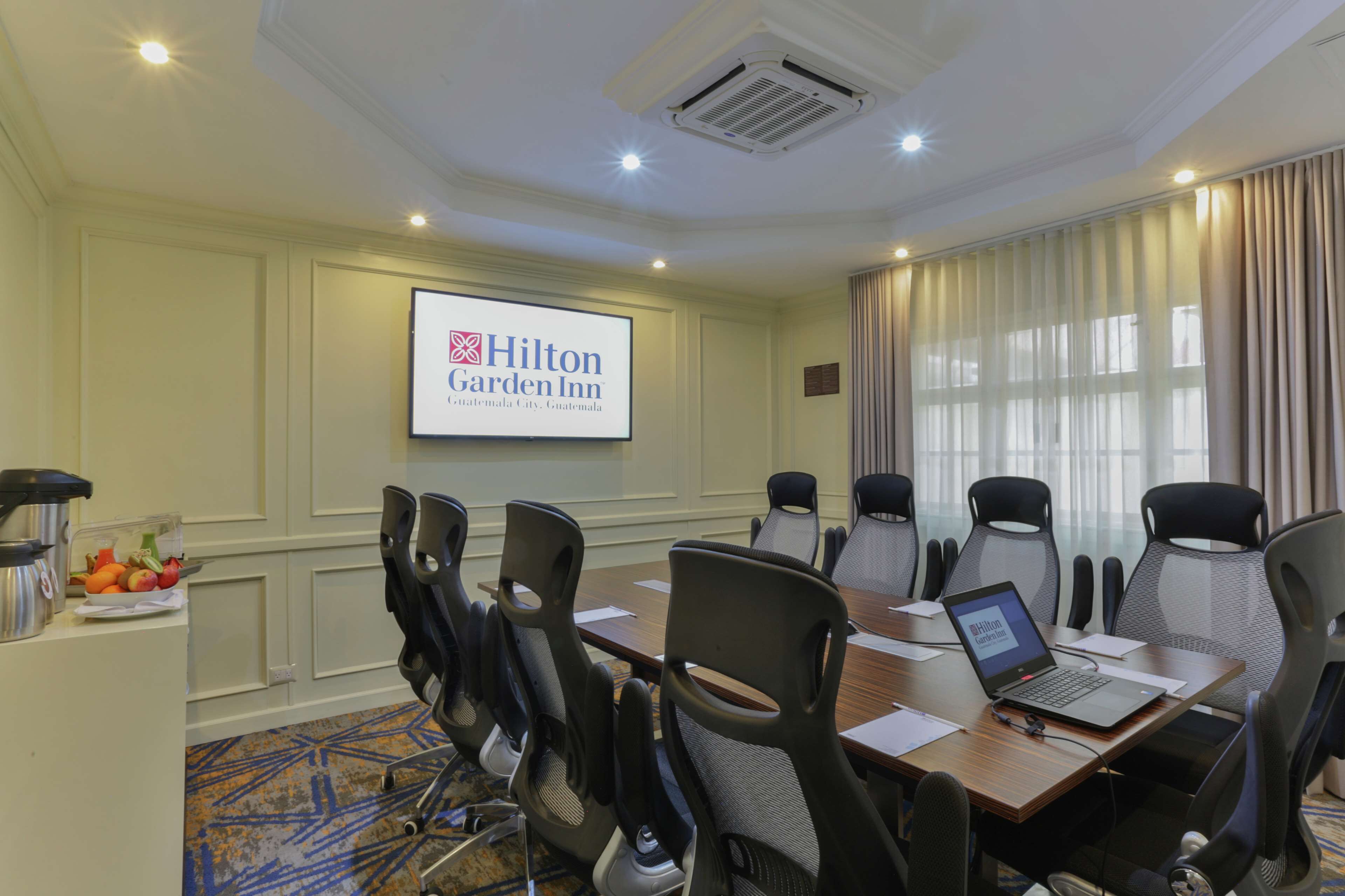 A conference room with a Hilton Garden Inn sign, a laptop on the table, and a fruit bowl on the side.