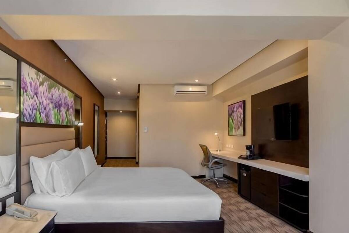 Een hotelkamer met een bed, nachtkastje, bureau, stoel en kunstwerken aan de muren.