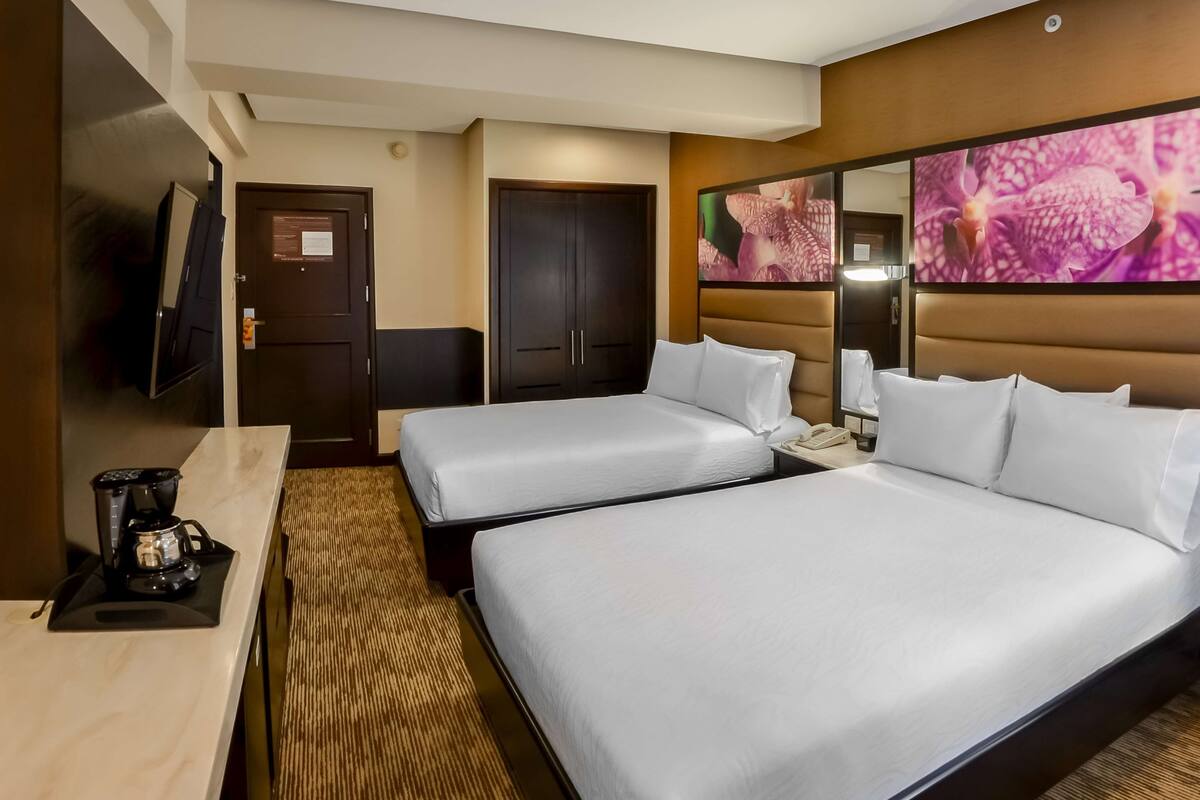 Een hotelkamer met twee bedden, een koffiezetapparaat, een televisie en een groot bloemwerk aan de muur.