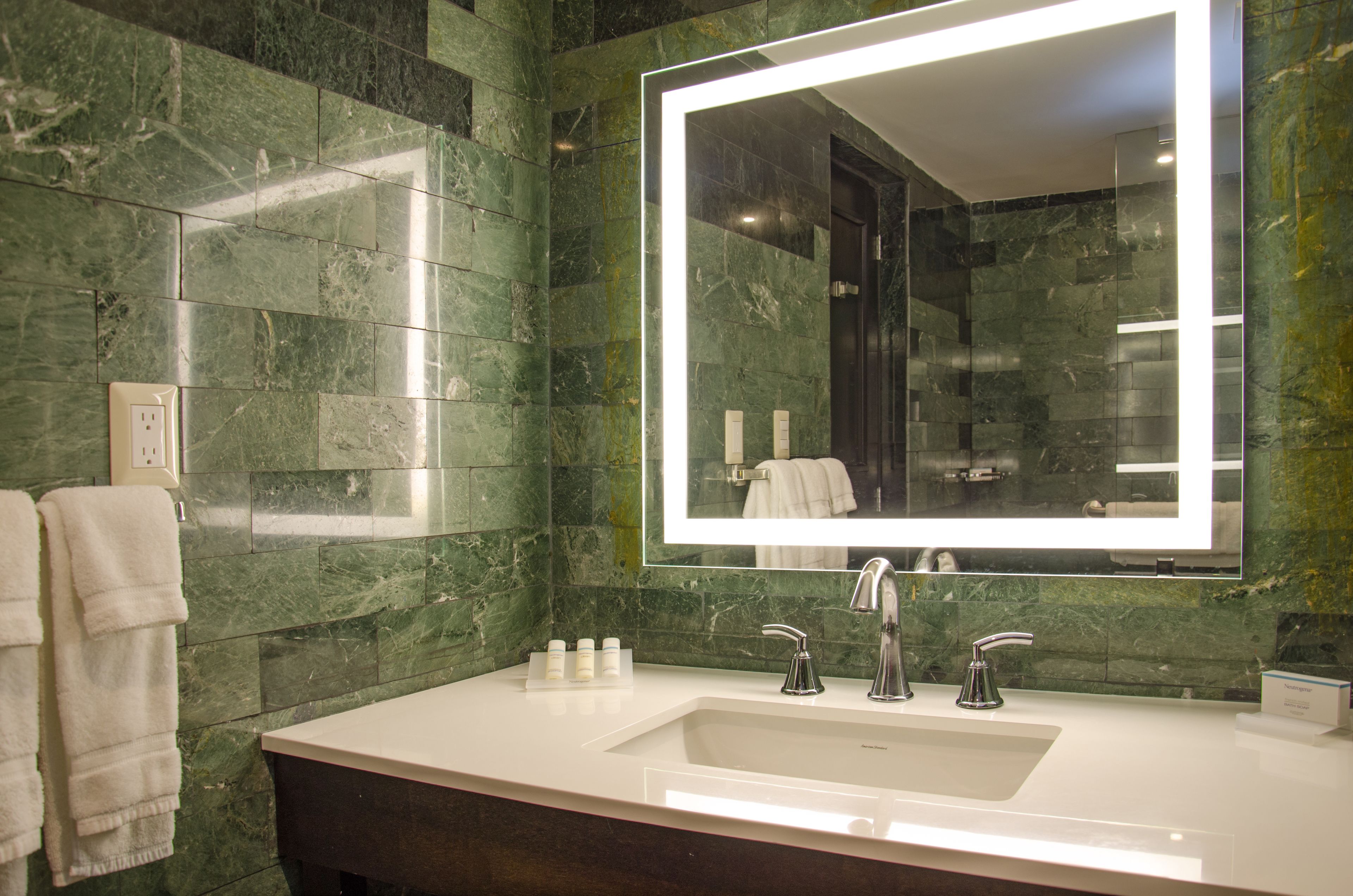 A bathroom with a white sink, two faucets, a large mirror, and green marble walls.