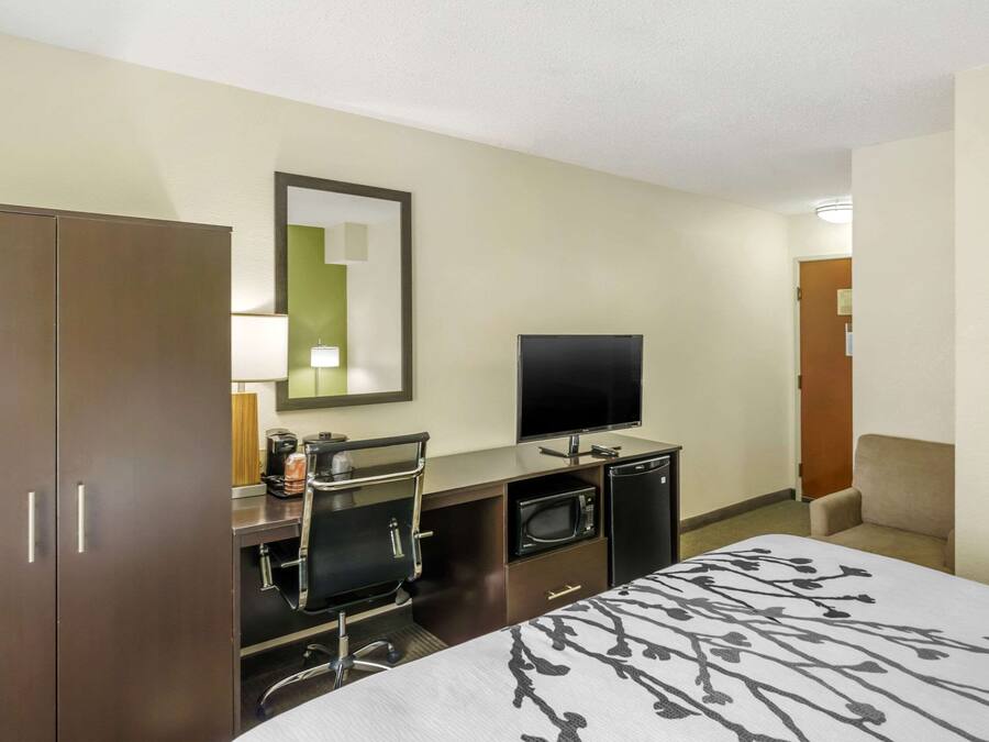 Habitación de hotel con cama, escritorio, televisor de pantalla plana, microondas, cafetera y una silla.