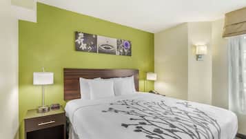 A hotel room with a bed, two bedside tables with lamps, a nightstand, a wall-mounted artwork, and a window with curtains.