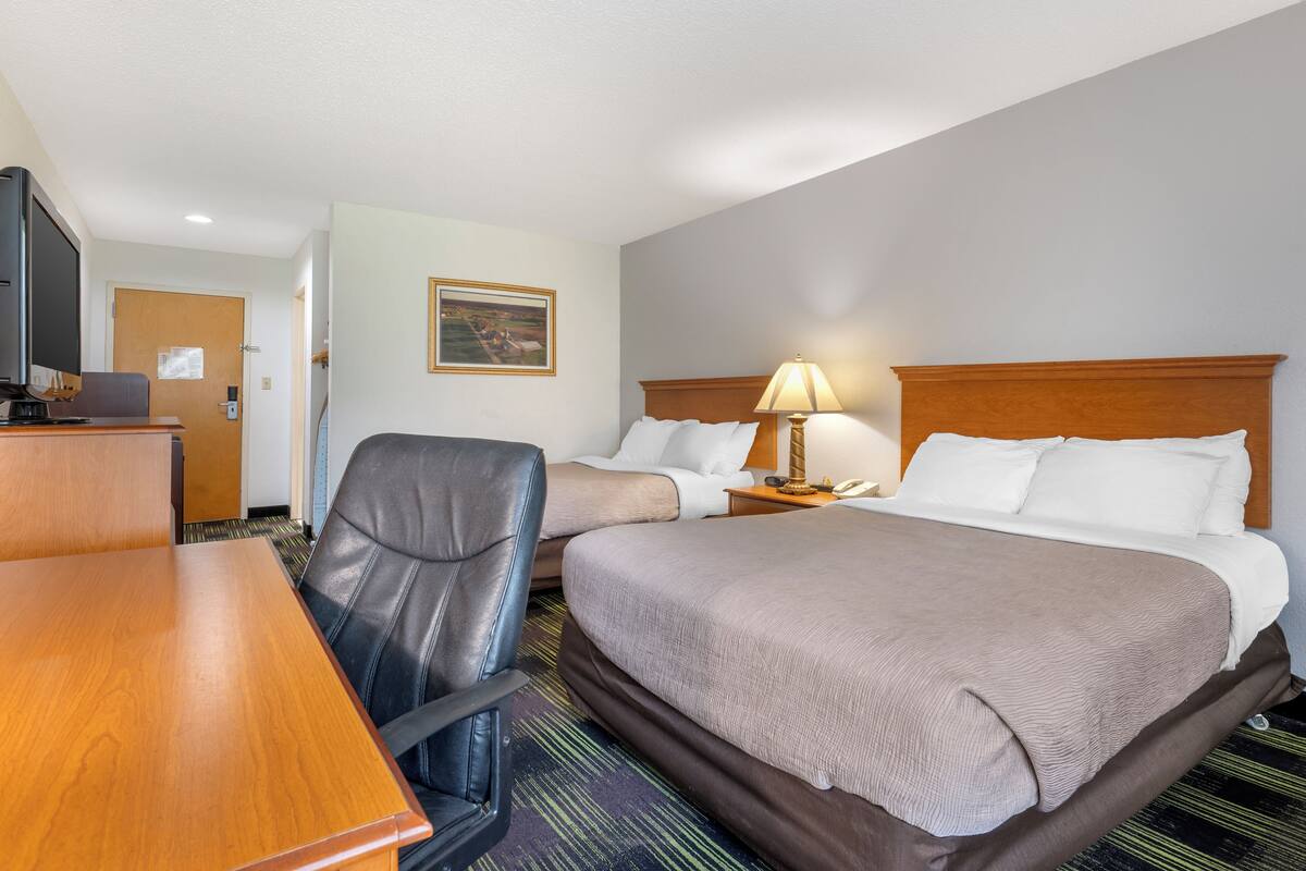 A hotel room with two beds, a desk, a chair, a television, and a painting on the wall.