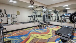 Un gimnasio con equipamiento de ejercicio, una cinta de correr y un espejo grande.