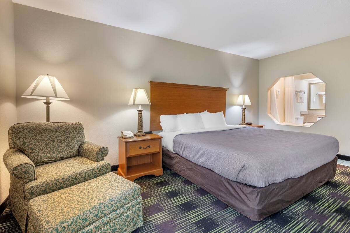 A hotel room with a bed, two bedside tables with lamps, a chair, and a large mirror on the wall.