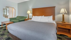 Habitación de hotel con una cama grande, dos mesitas de noche, un sillón verde y un espejo en la pared.