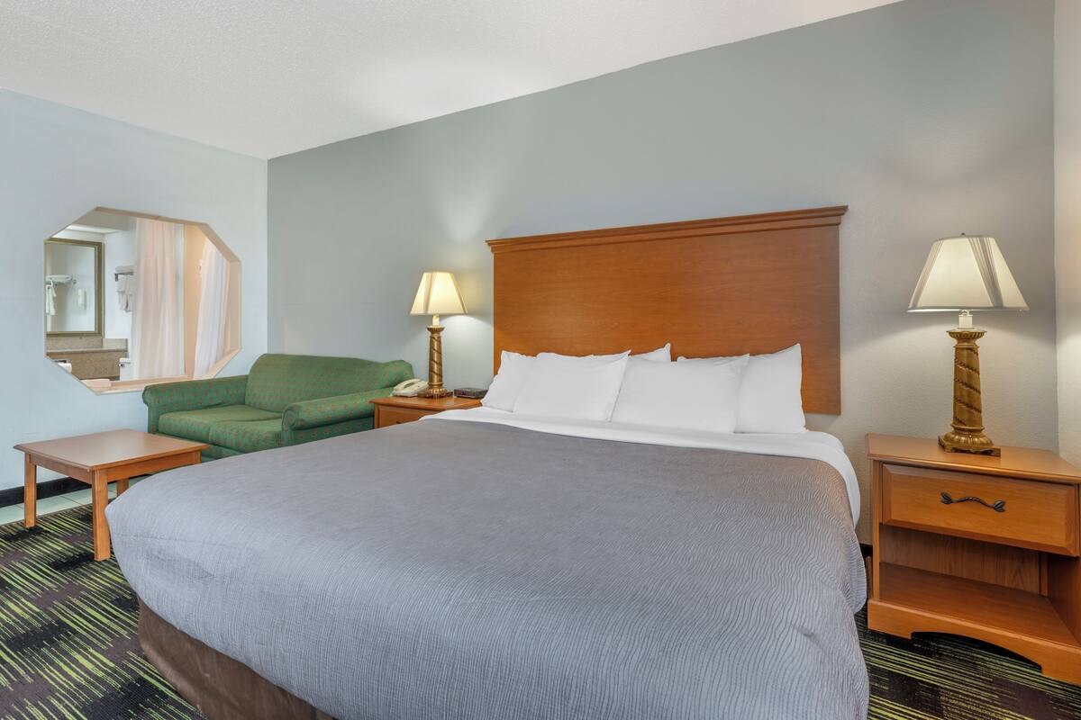 A hotel room with a large bed, two bedside tables, a green armchair, and a mirror on the wall.