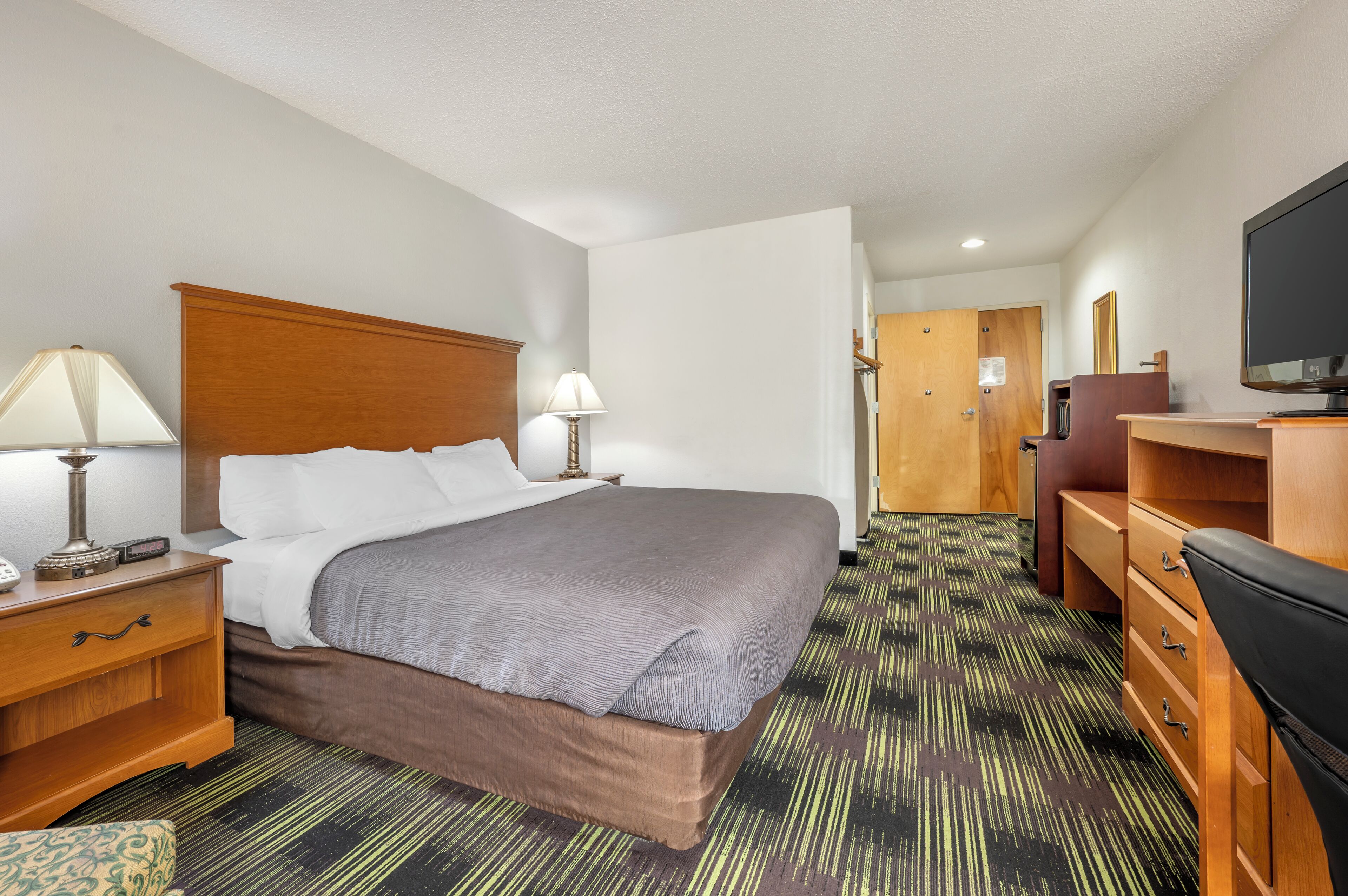A hotel room with a large bed, two bedside tables with lamps, a television, a desk, and a wardrobe.