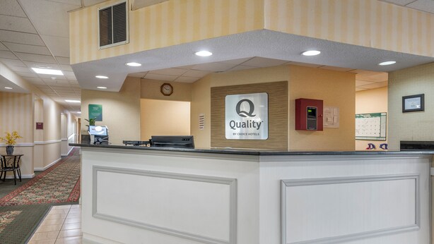 Mostrador de recepción de hotel con un cartel que dice "Quality by Choice Hotels", un reloj y un calendario en la pared.