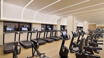 Un gimnasio con varias cintas de correr y elípticas, cada una equipada con pantallas digitales.